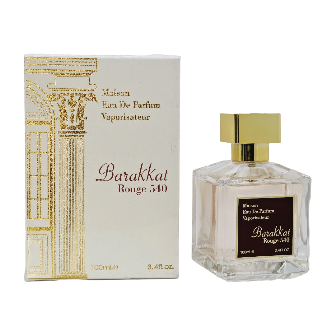 A bottle of Barakkat Rouge 540 Unisex Eau De Parfum with its packaging box. The bottle is clear, showing the light amber-colored perfume liquid, and the box is adorned with gold and brown designs indicating the luxury brand 'Maison'.